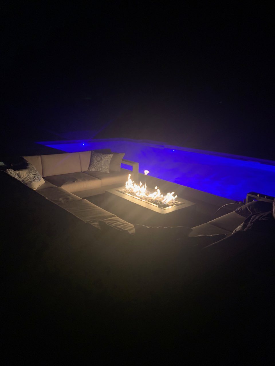 Custom gas fire table burning at night beside a pool